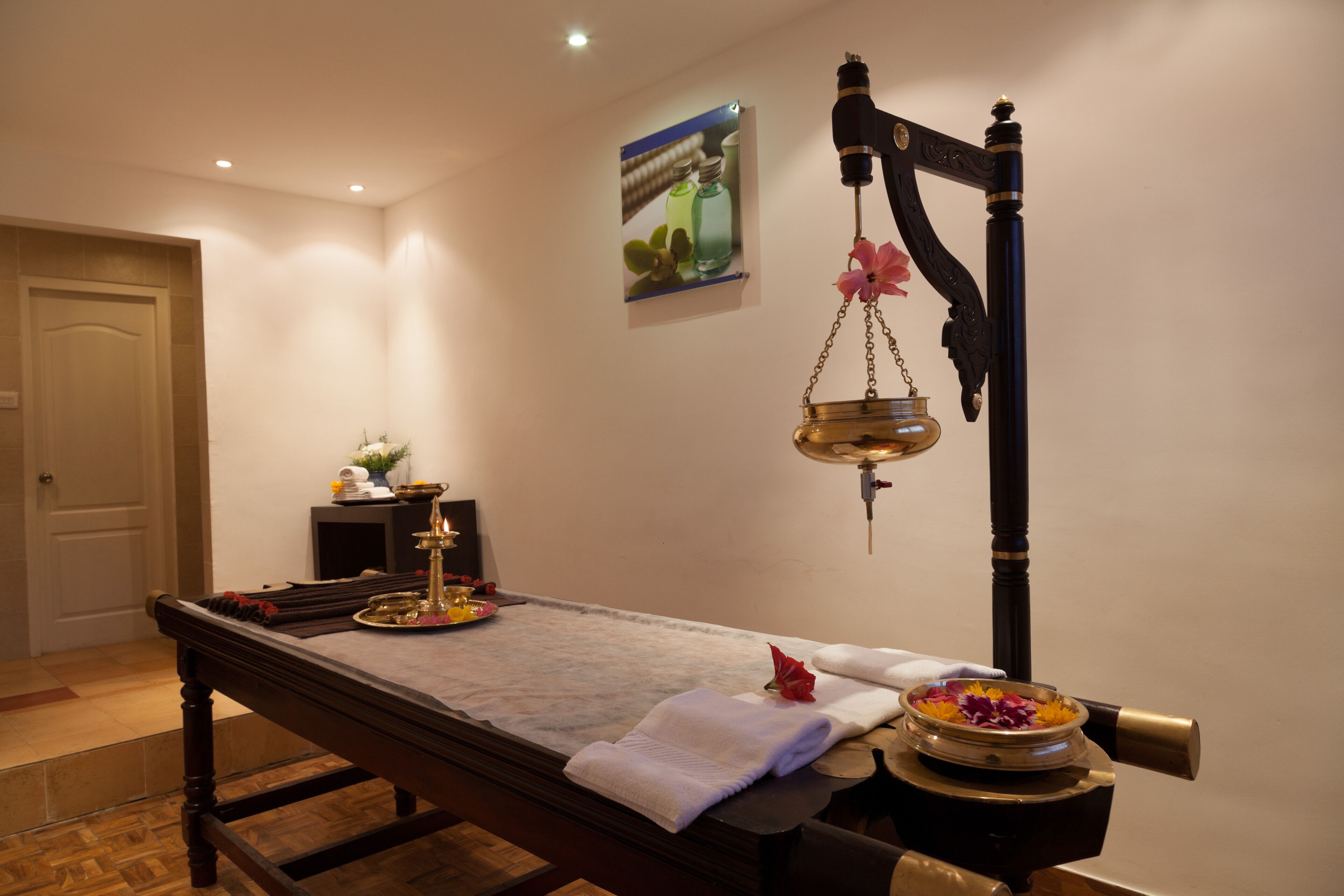 A massage table with a towel, a small table with a flower, and a wall-mounted massage device.