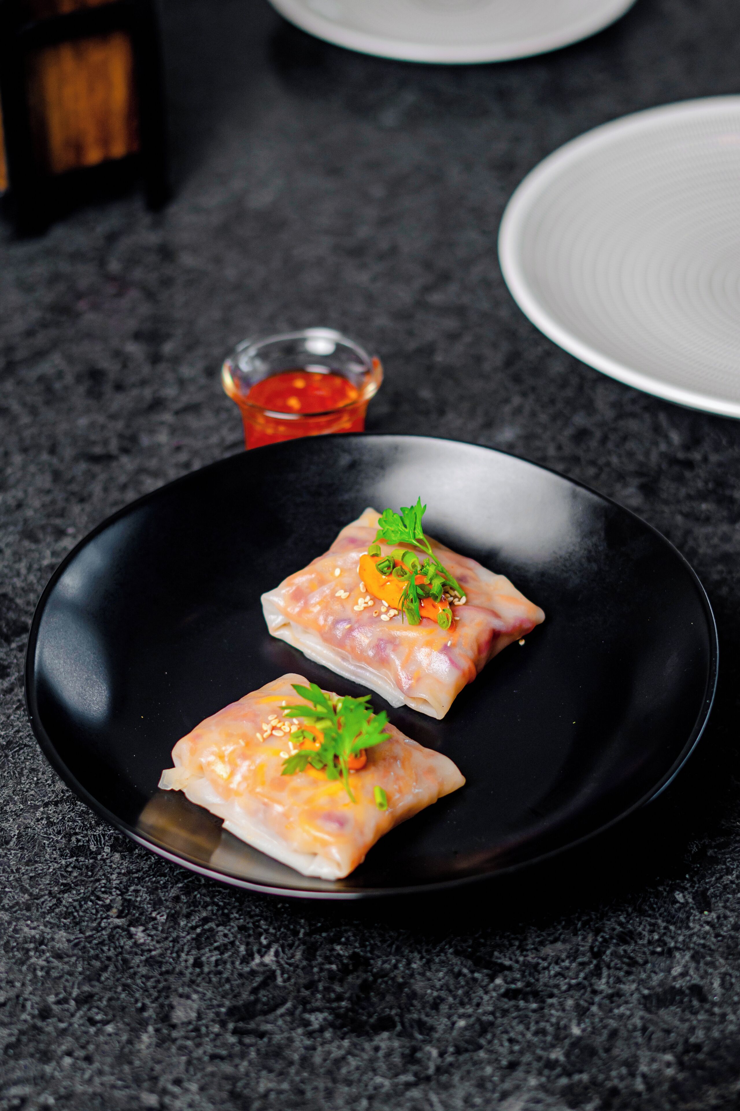 A black plate with two spring rolls garnished with green herbs and sesame seeds.