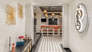 A modern hotel corridor with white brick walls, a patterned floor, and a seating area with a sofa and chairs.