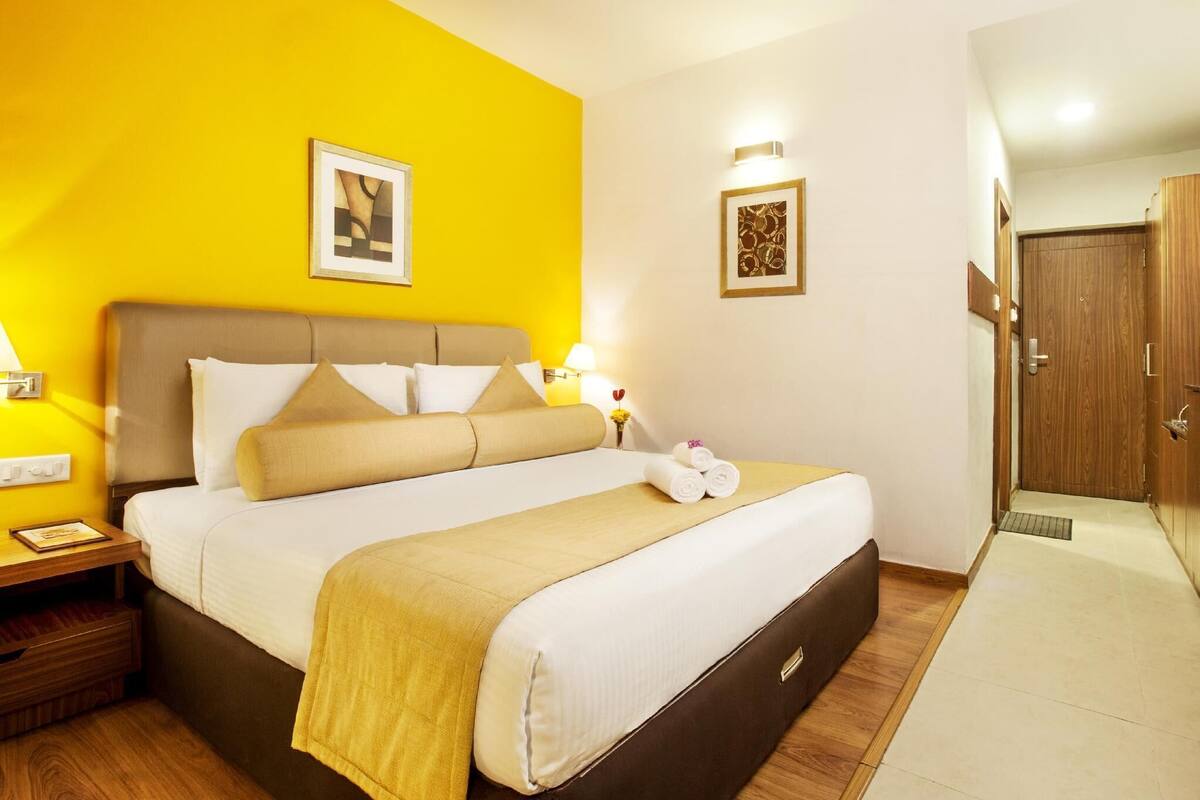 Une chambre d’hôtel avec un lit, des tables de chevet, une commode, une porte en bois et un mur orné de deux tableaux encadrés.