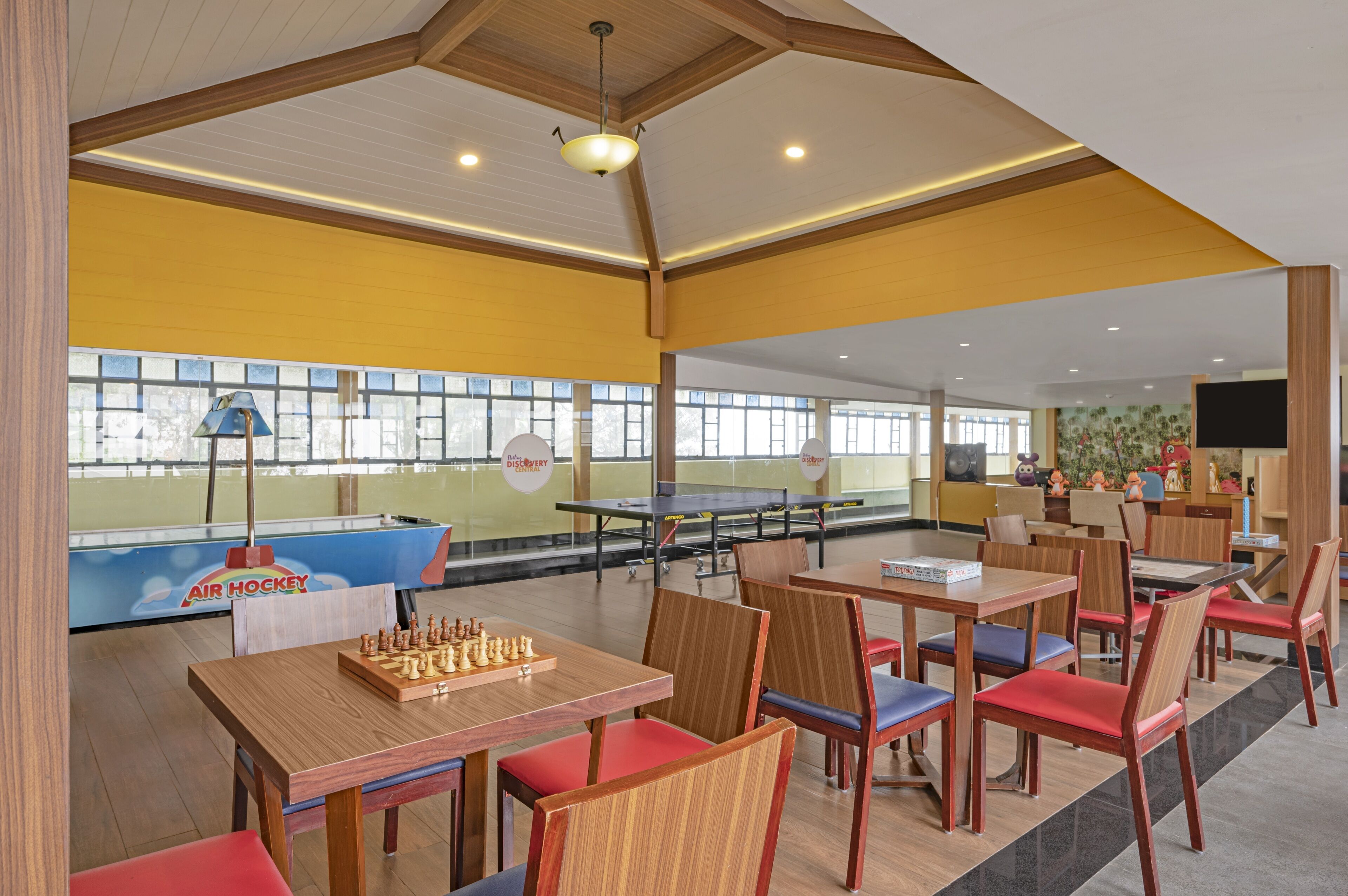 A bowling alley with tables and chairs, a ping pong table, and a large window with a view of trees.