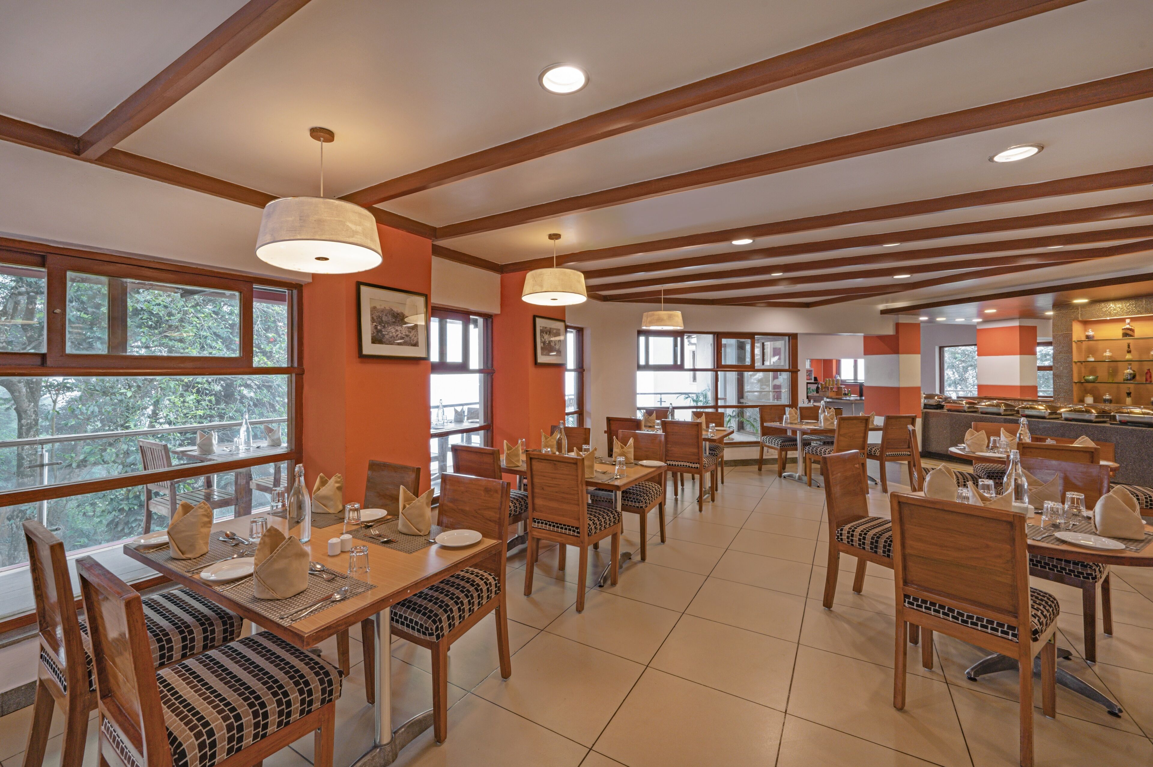A spacious dining area with wooden tables and chairs, large windows, and pendant lighting.