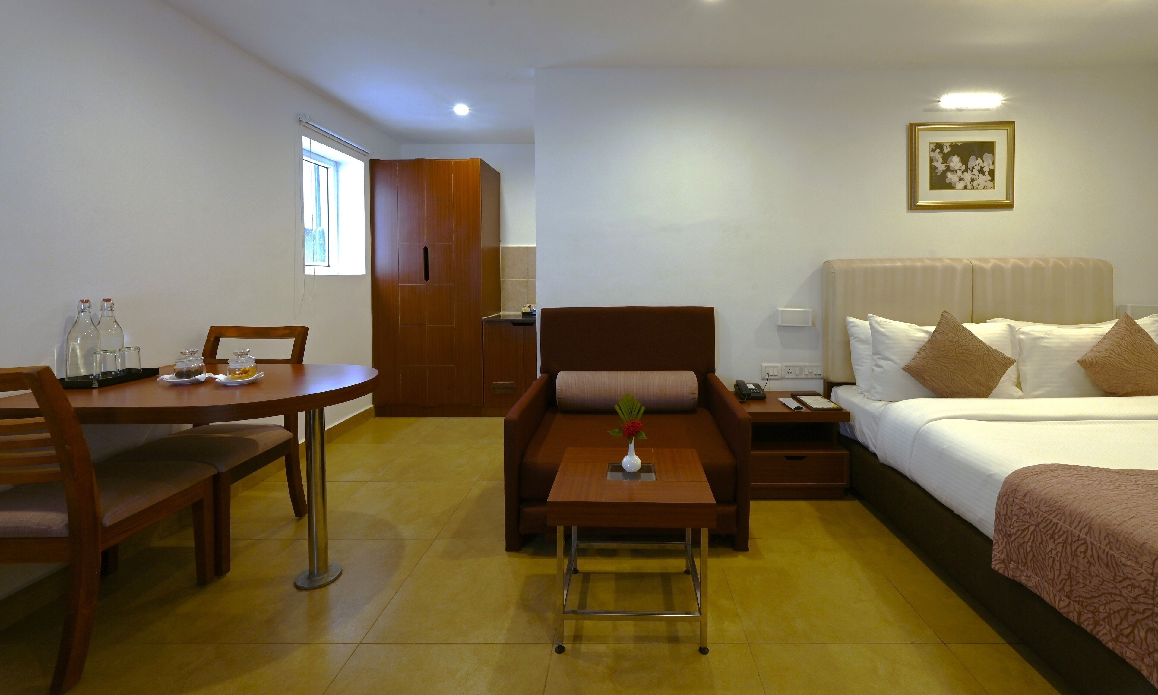 A hotel room with a bed, a desk, a chair, a small table, and a nightstand.