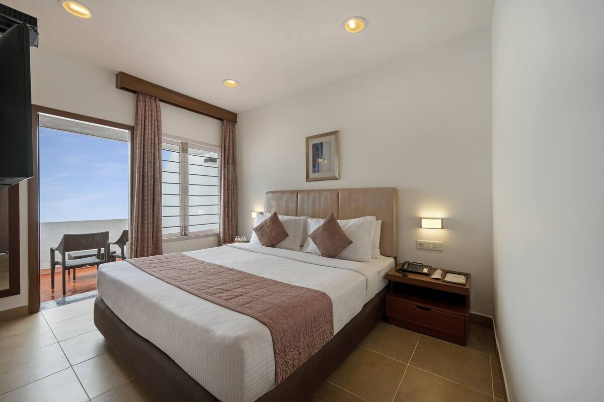 Une chambre d’hôtel avec un grand lit, un bureau avec un téléphone et une vue sur la mer, accessible par une porte coulissante.