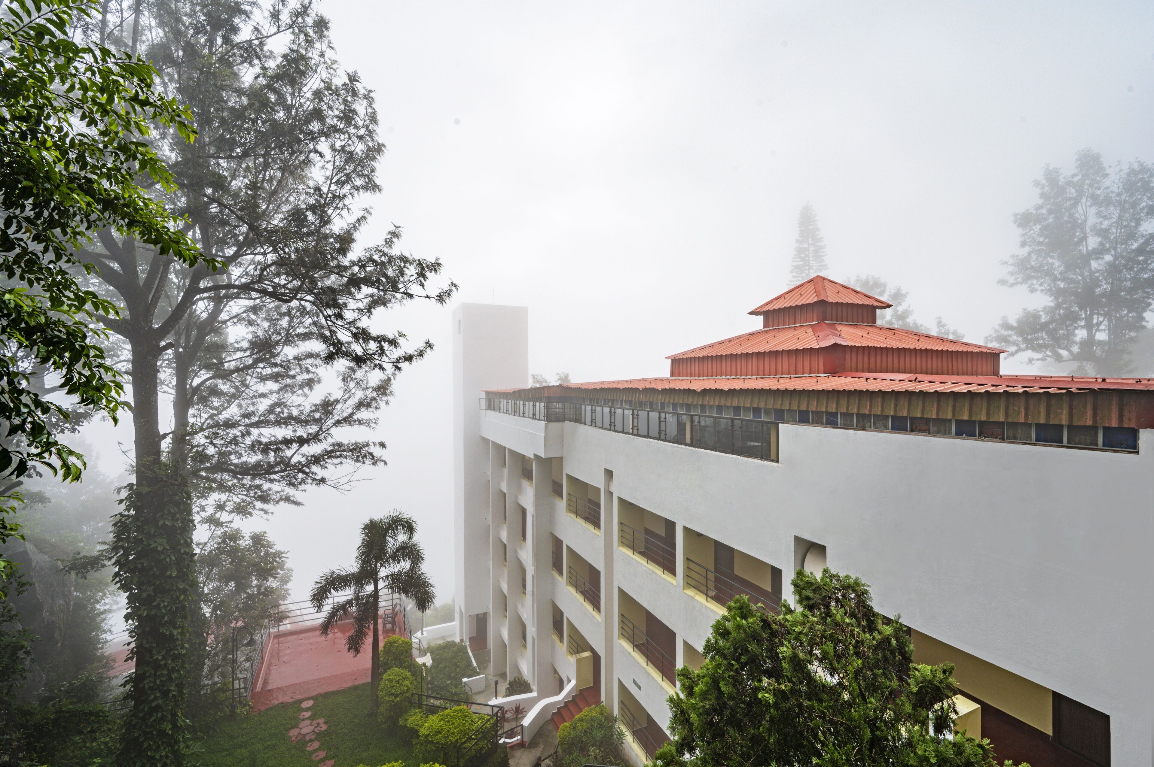 Un edificio de varios pisos con techo rojo, rodeado de árboles y neblina.