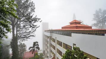 Un edificio de varios pisos con techo rojo, rodeado de árboles y neblina.