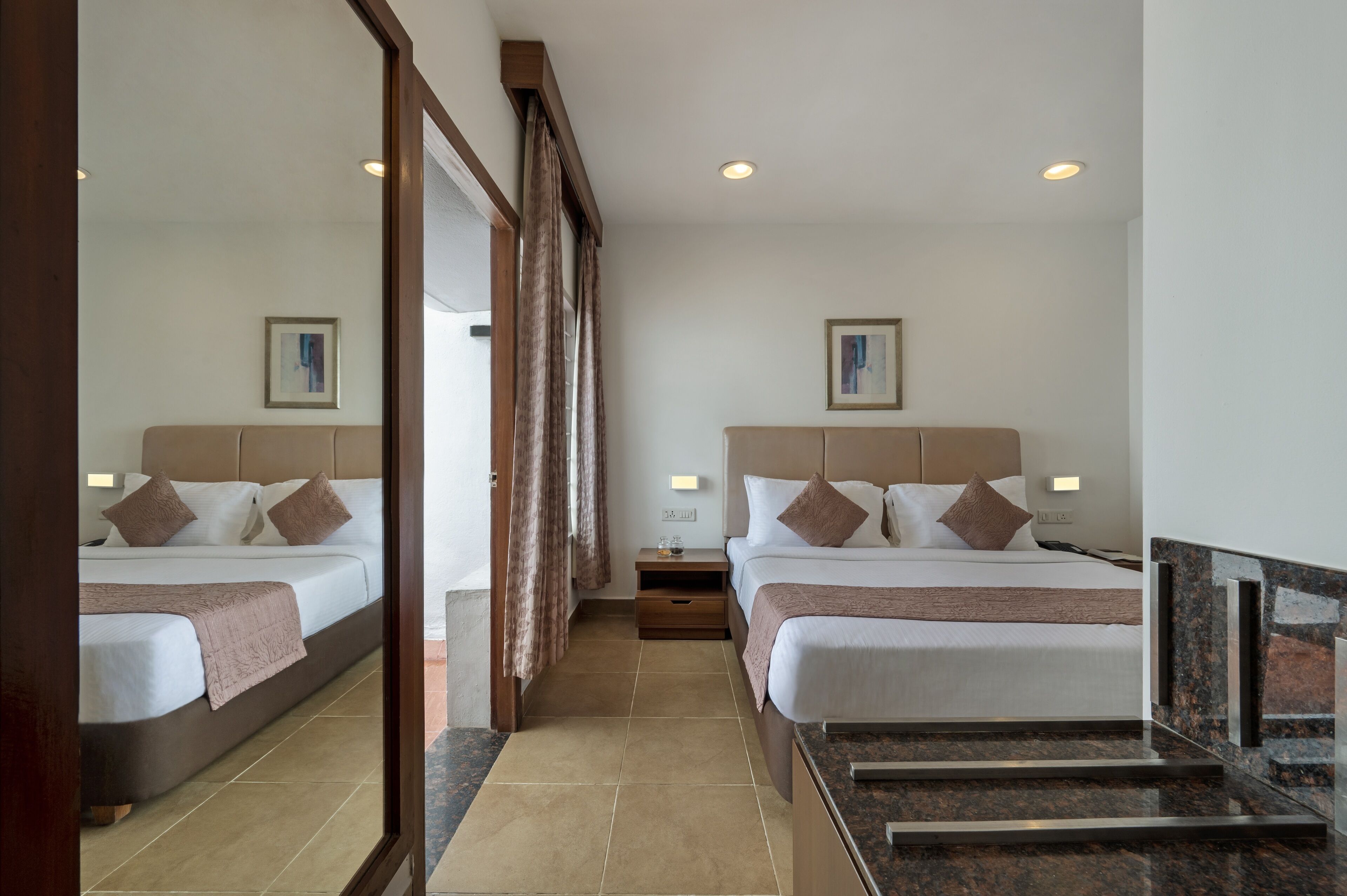 A hotel room with two beds, a mirror, a nightstand, and a view of the outside.