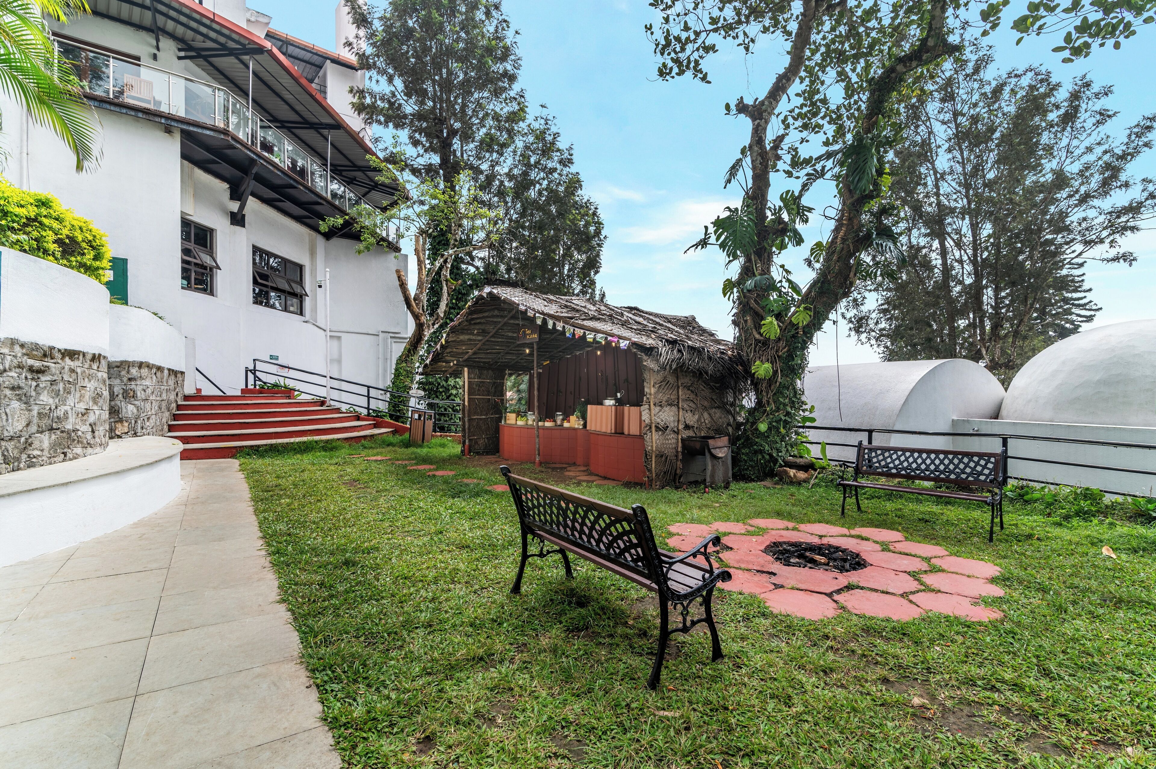 A courtyard with a bench, a small hut, and a staircase leading to a building.