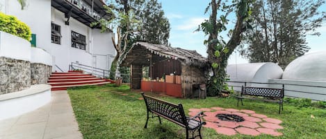 A courtyard with a bench, a small hut, and a staircase leading to a building.