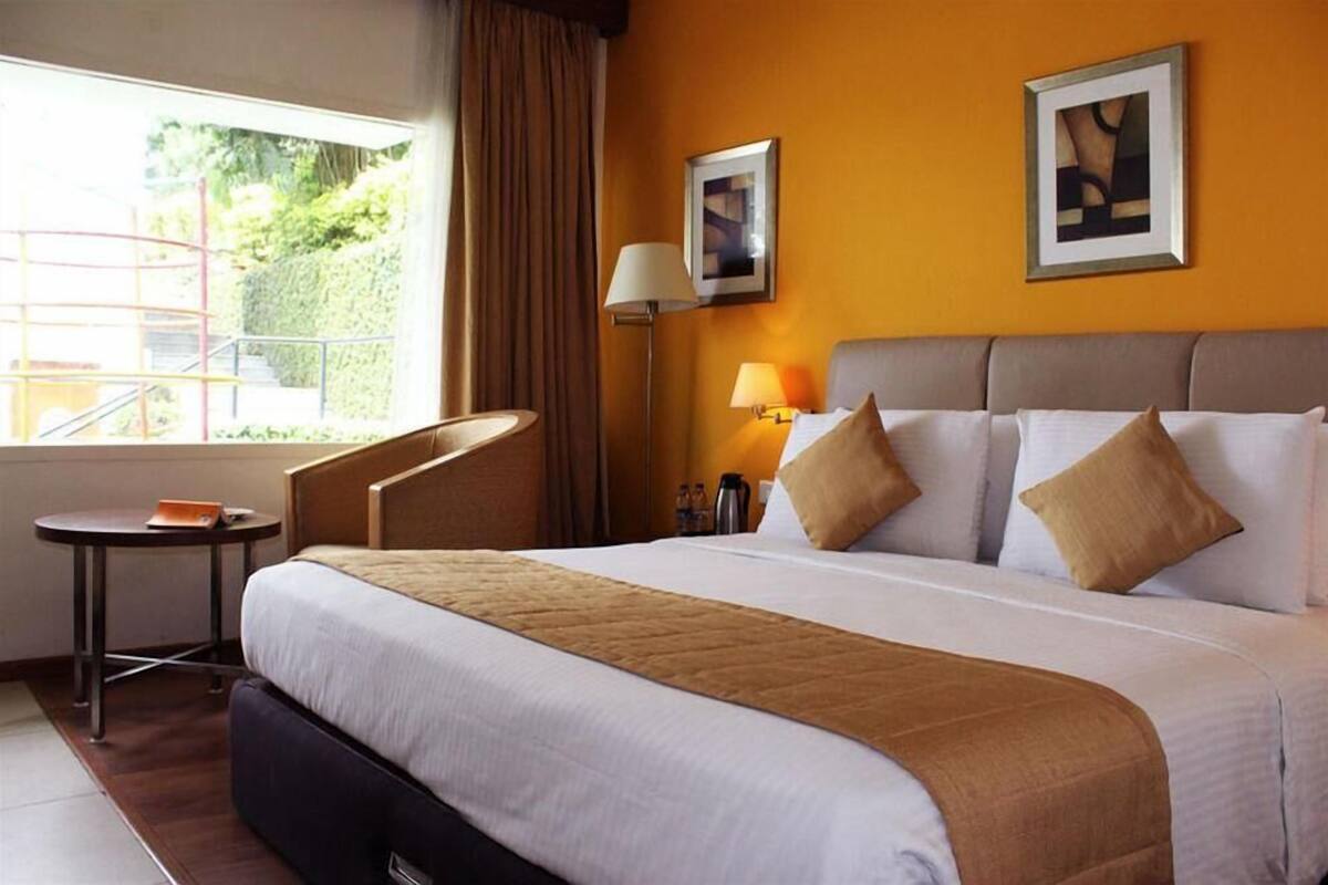 Une chambre d’hôtel avec un lit, une chaise, une petite table, une lampe et deux tableaux encadrés au mur.