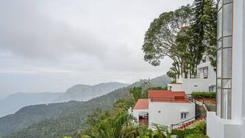 A modern building with a red roof, surrounded by lush greenery and mountains in the background.