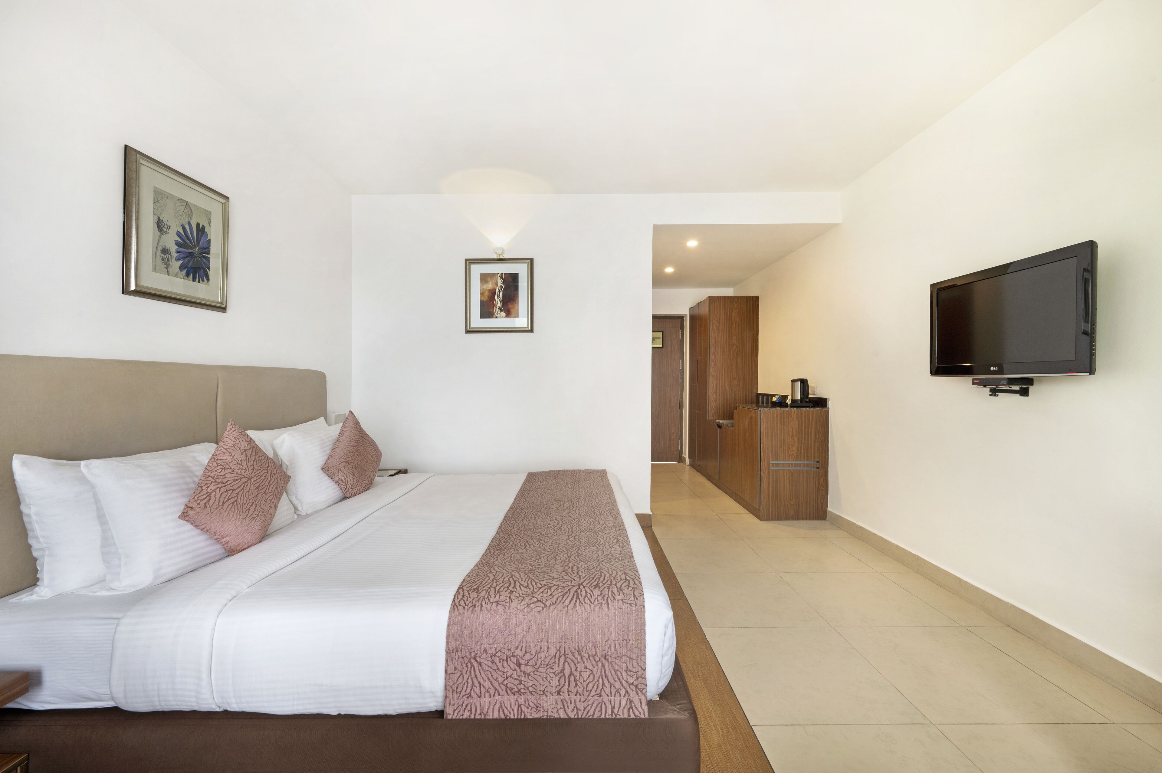 A hotel room with a large bed, a flat-screen TV mounted on the wall, and a wooden cabinet in the background.