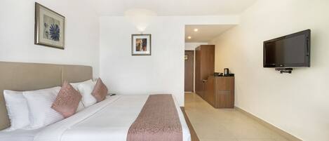A hotel room with a large bed, a flat-screen TV mounted on the wall, and a wooden cabinet in the background.