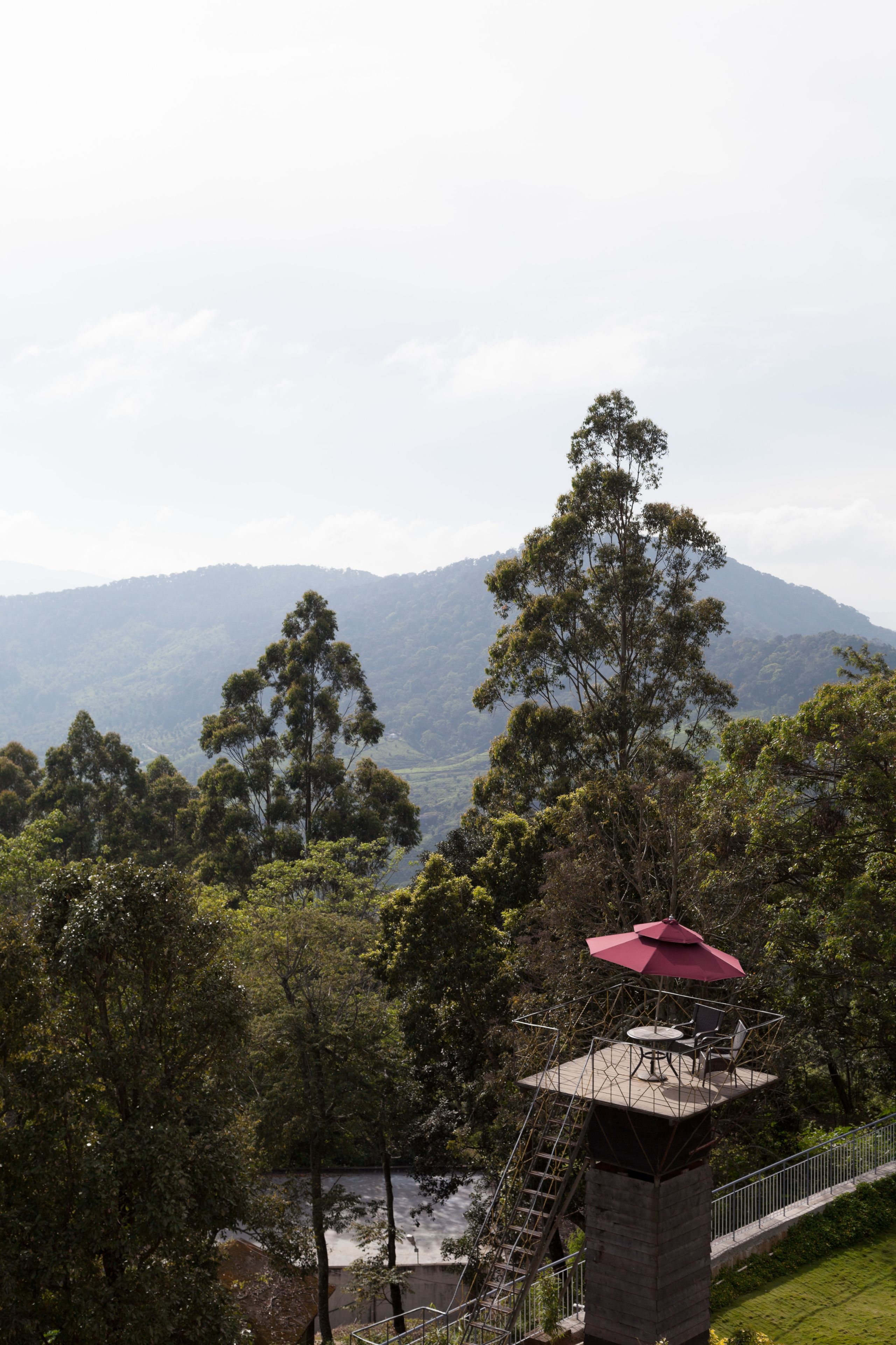 A lookout tower with a red umbrella, surrounded by lush greenery and a river.