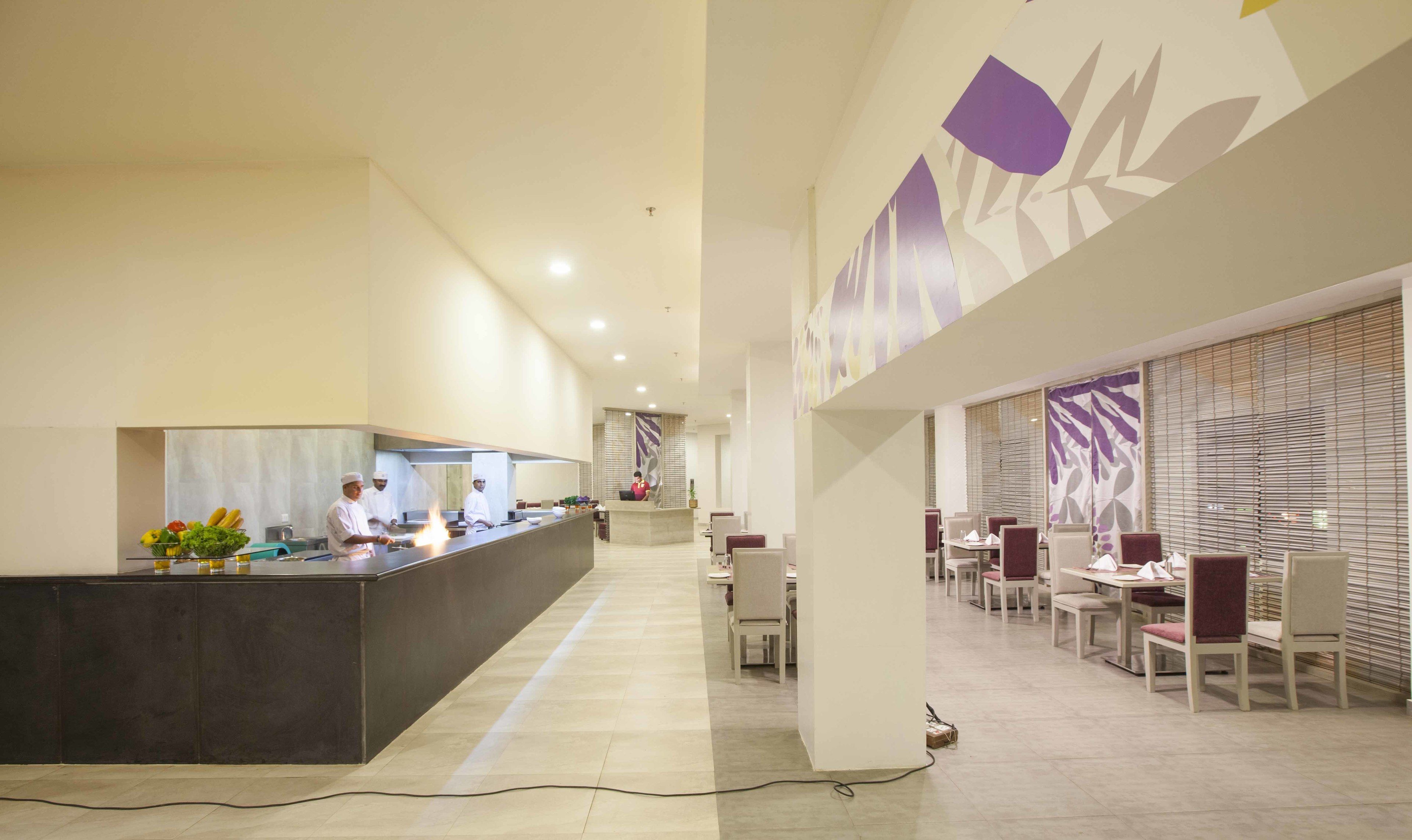 A modern hotel lobby with a reception desk, a dining area with tables and chairs, and a kitchen area with chefs.