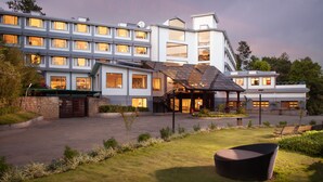 A modern hotel with multiple floors, a covered entrance, and a well-maintained outdoor area with a seating area. - Sterling Munnar (Devikolam)