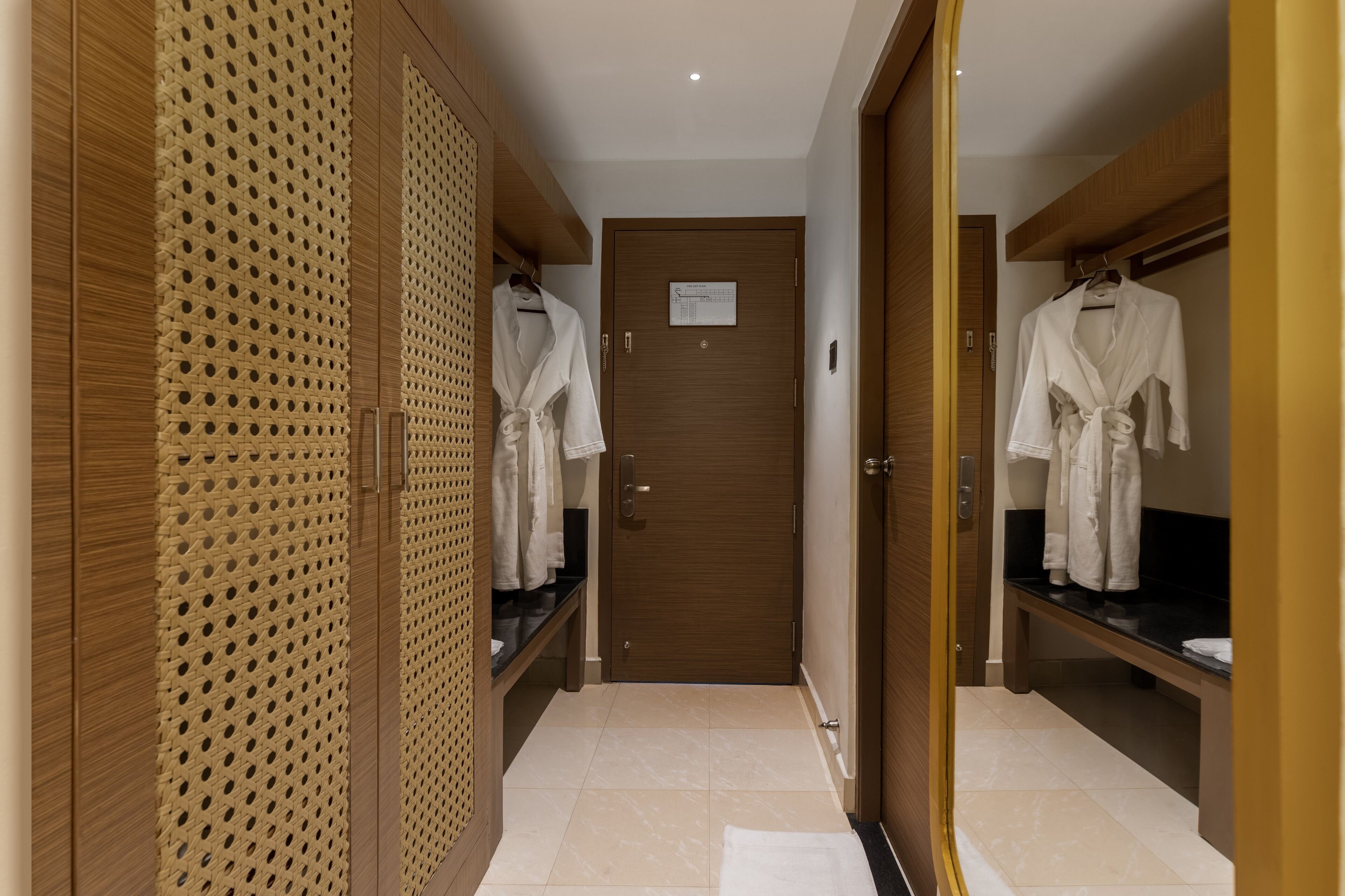 Un pasillo de hotel con armarios de madera, una puerta central y dos ganchos para bata en la pared derecha.
