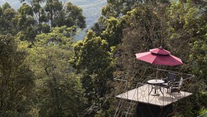 A small outdoor seating area with a table and chairs, surrounded by dense foliage and trees. - Sterling Munnar (Devikolam)