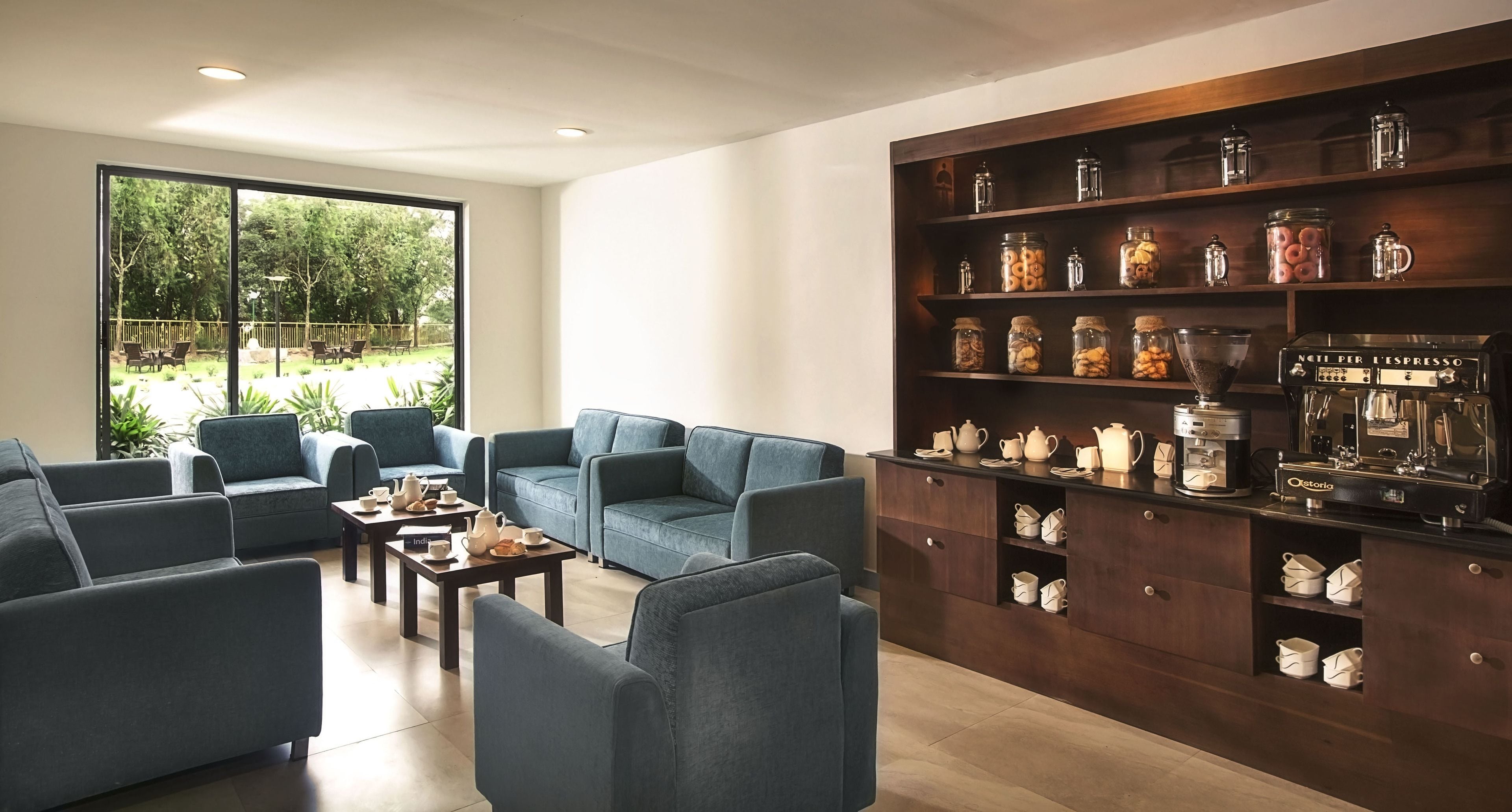 A modern living room with blue sofas, a coffee machine, and shelves with jars.