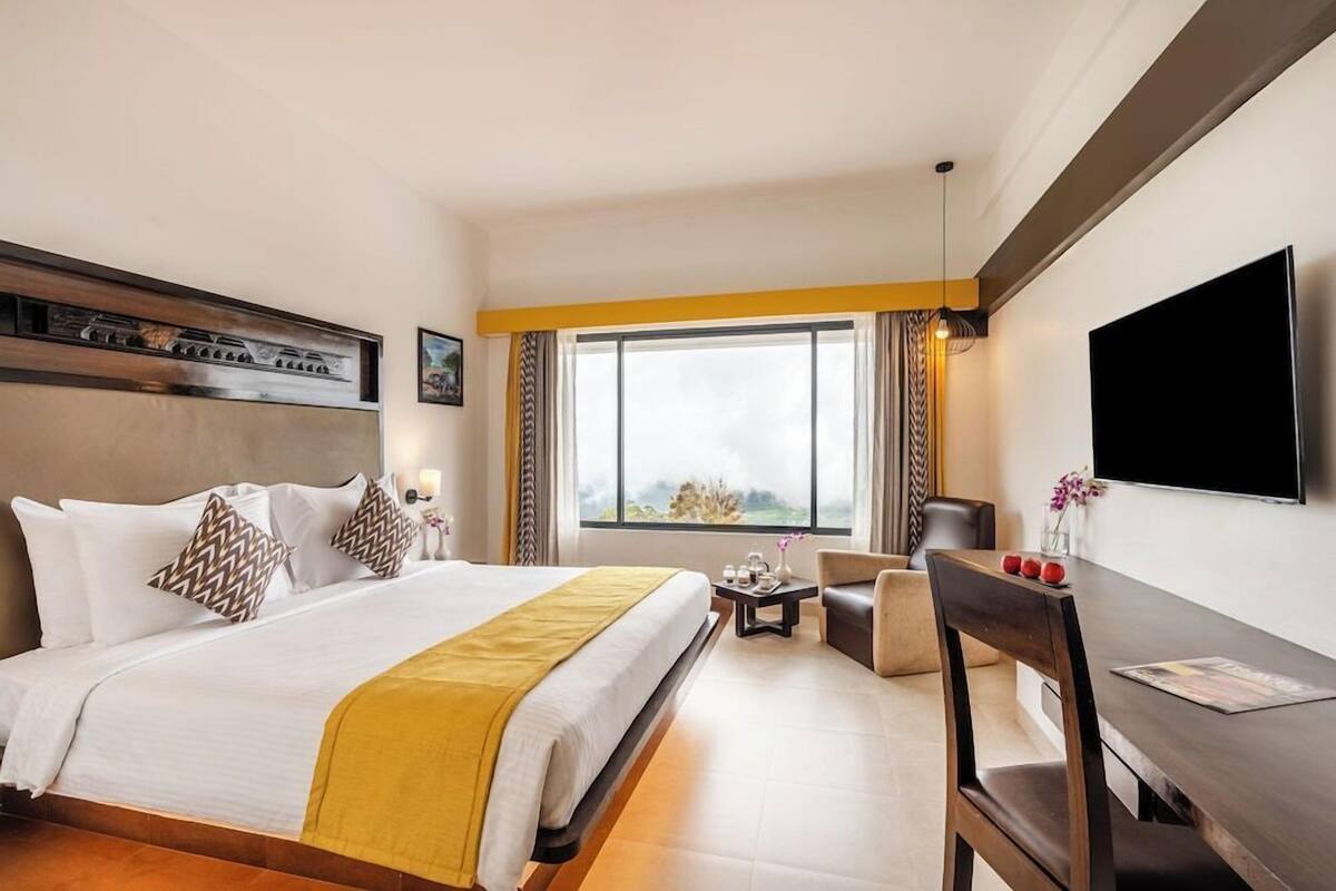 A hotel room with a bed, a desk, a chair, a TV, and a window with curtains.