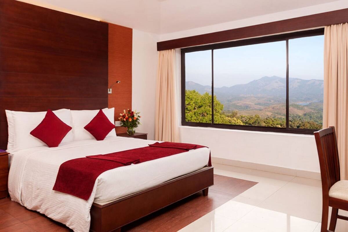 A modern bedroom with a large bed, wooden headboard, a desk, and a view of mountains.