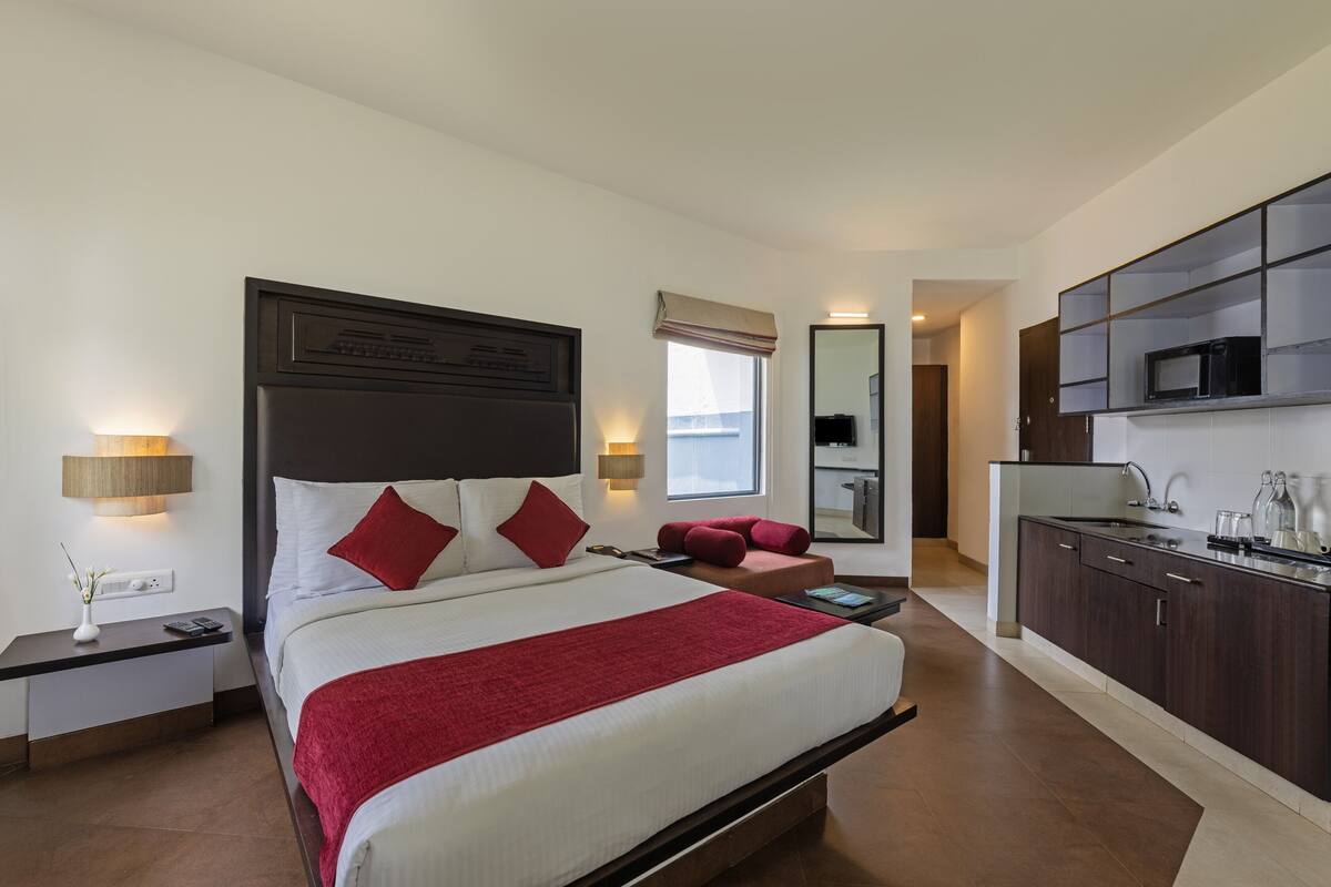 A hotel room with a large bed, a desk, a nightstand, a microwave, and a small kitchenette.