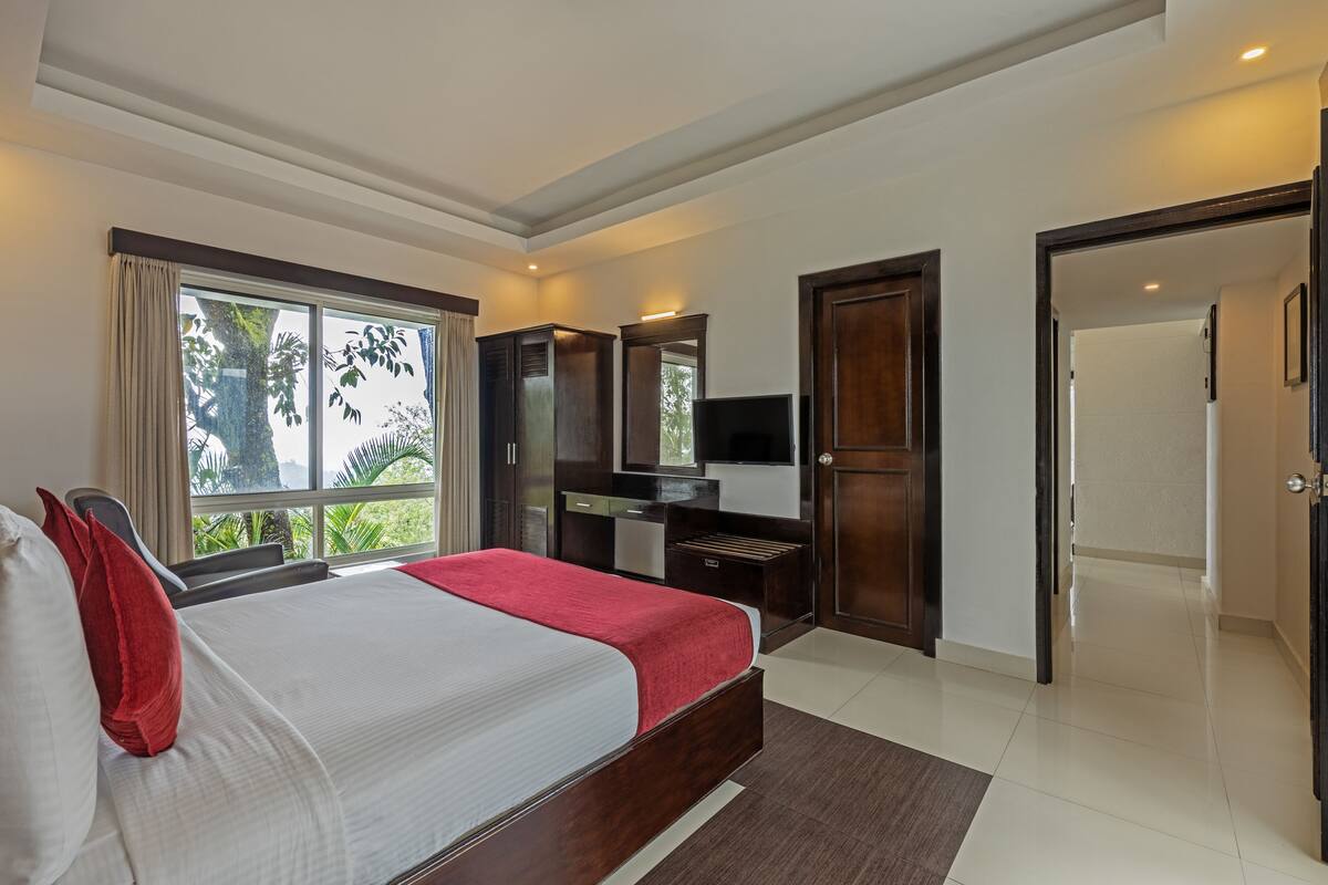 A bedroom with a large bed, a TV, a wardrobe, and a bathroom door.