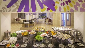 A buffet setup with various food items and utensils, a seating area with tables and chairs, and a decorative wall with abstract patterns. - Sterling Munnar (Devikolam)