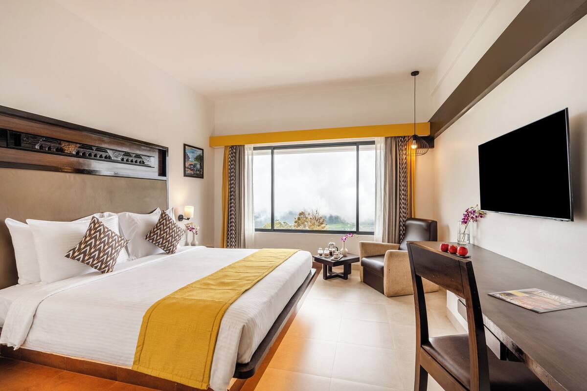 A hotel room with a large bed, a desk, a chair, a TV, and a window with curtains.