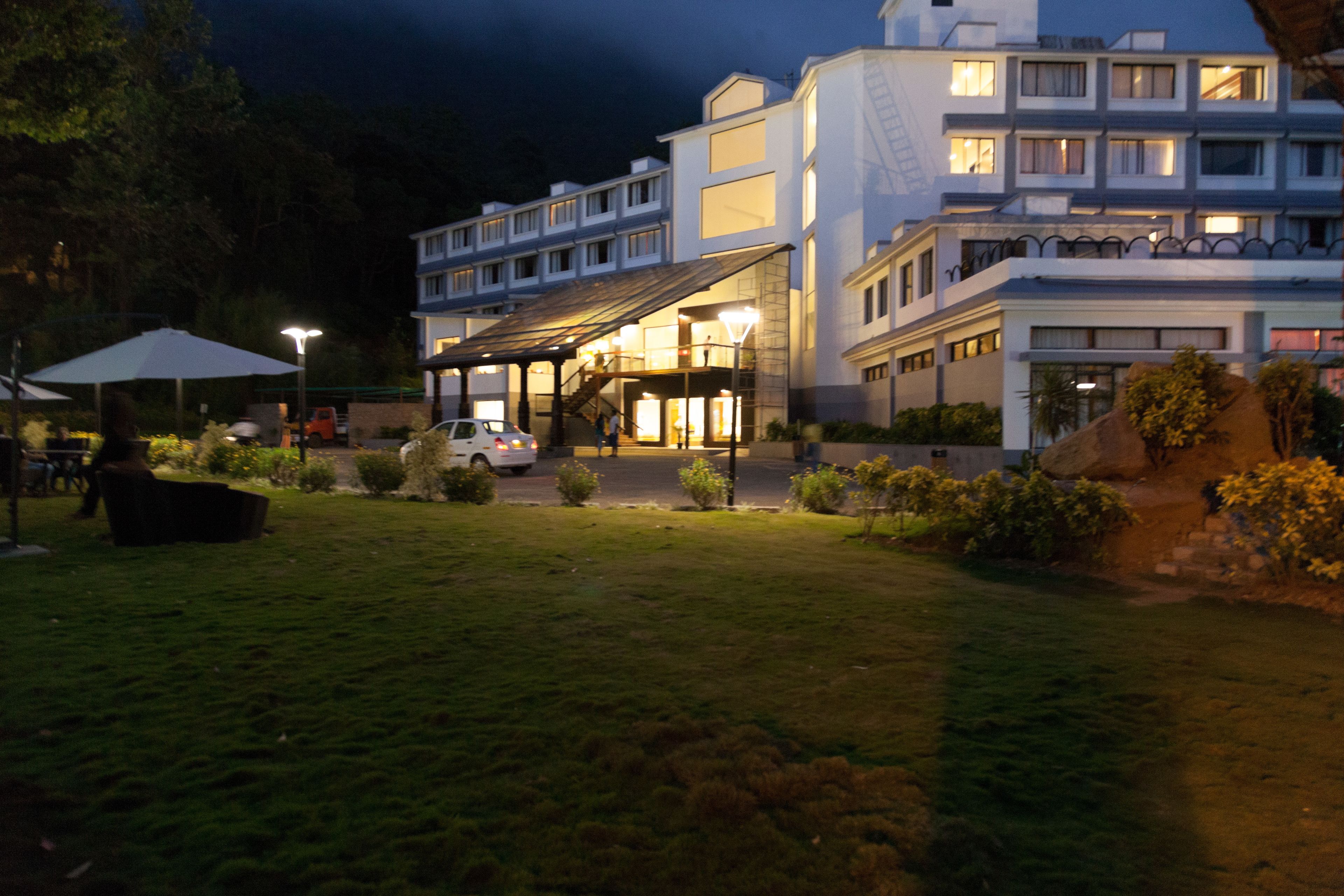 Un hotel con un espacio exterior cubierto, un coche aparcado delante y una entrada bien iluminada.