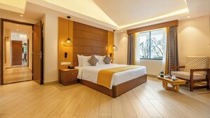 A modern hotel room with a large bed, wooden paneling, a sitting area with a chair, and a view of the outdoors through the window. - Sterling Munnar (Devikolam)