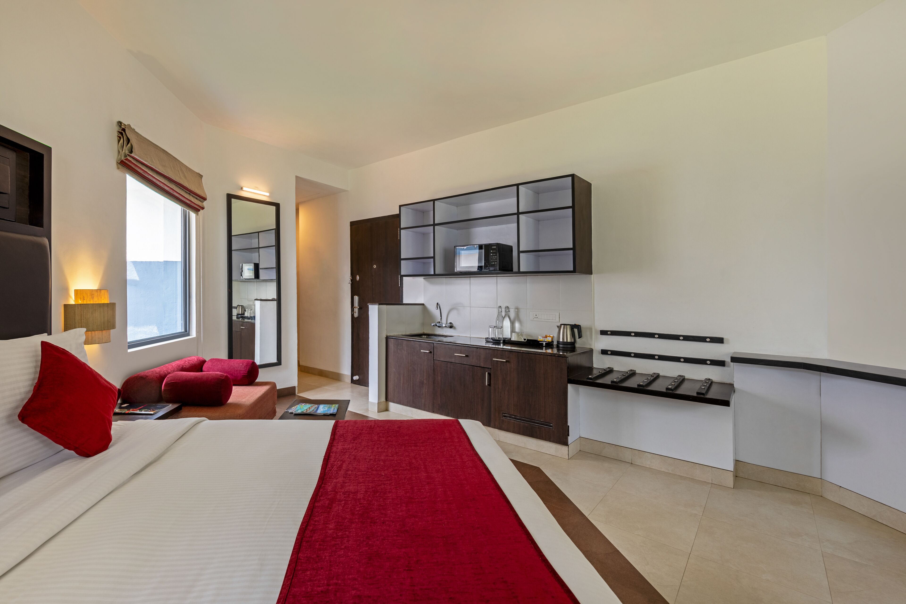 Een moderne hotelkamer met een groot bed, een rode plaid, een zithoekje, een kitchenette en een groot raam.