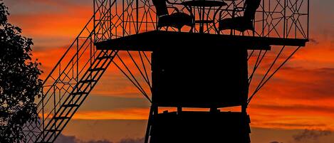Una alta torre de observación con una silla y una sombrilla, con vista a un atardecer.