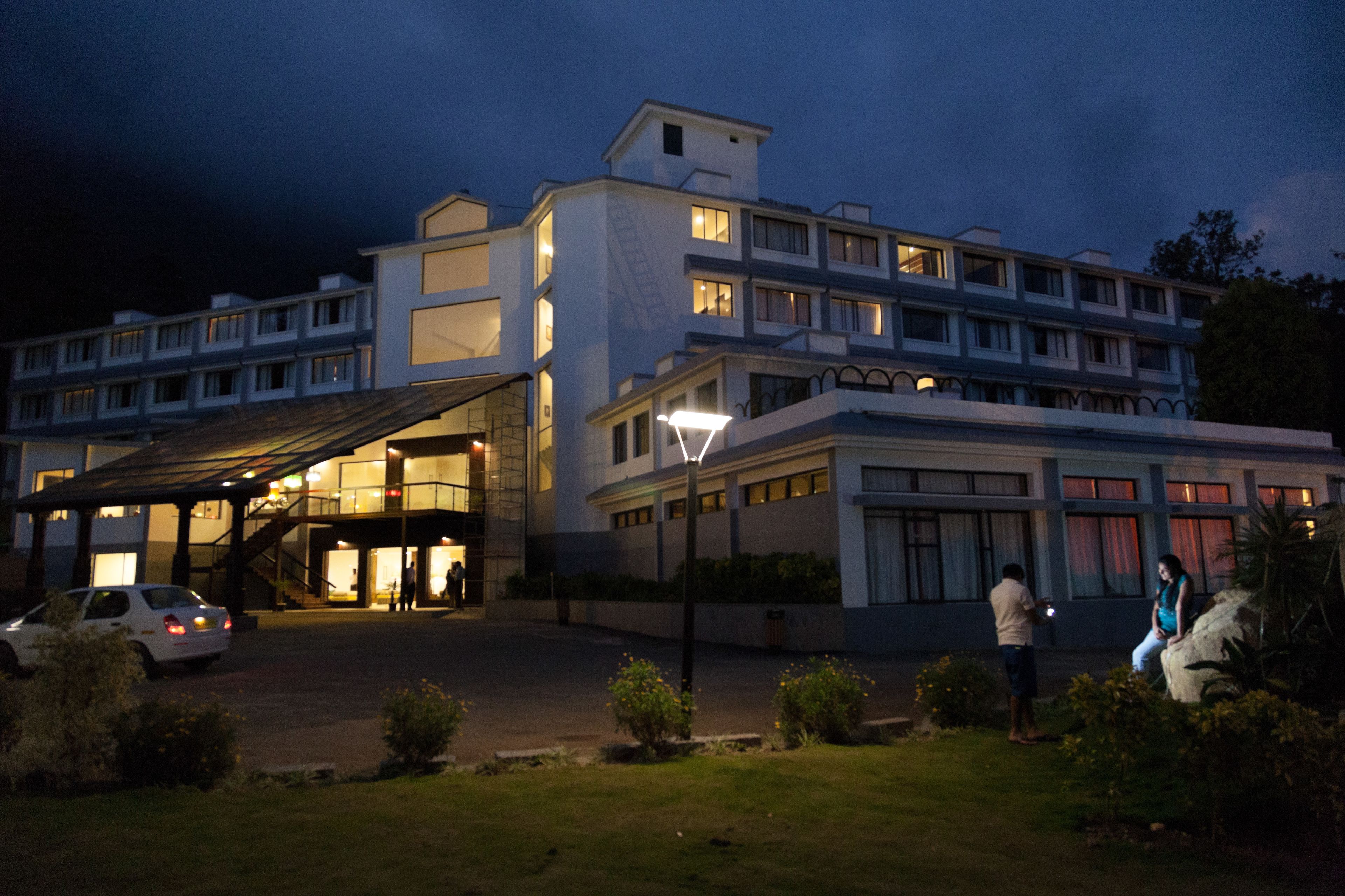 A multi-story hotel with a covered entrance, a car parked in front, and a well-lit building facade.