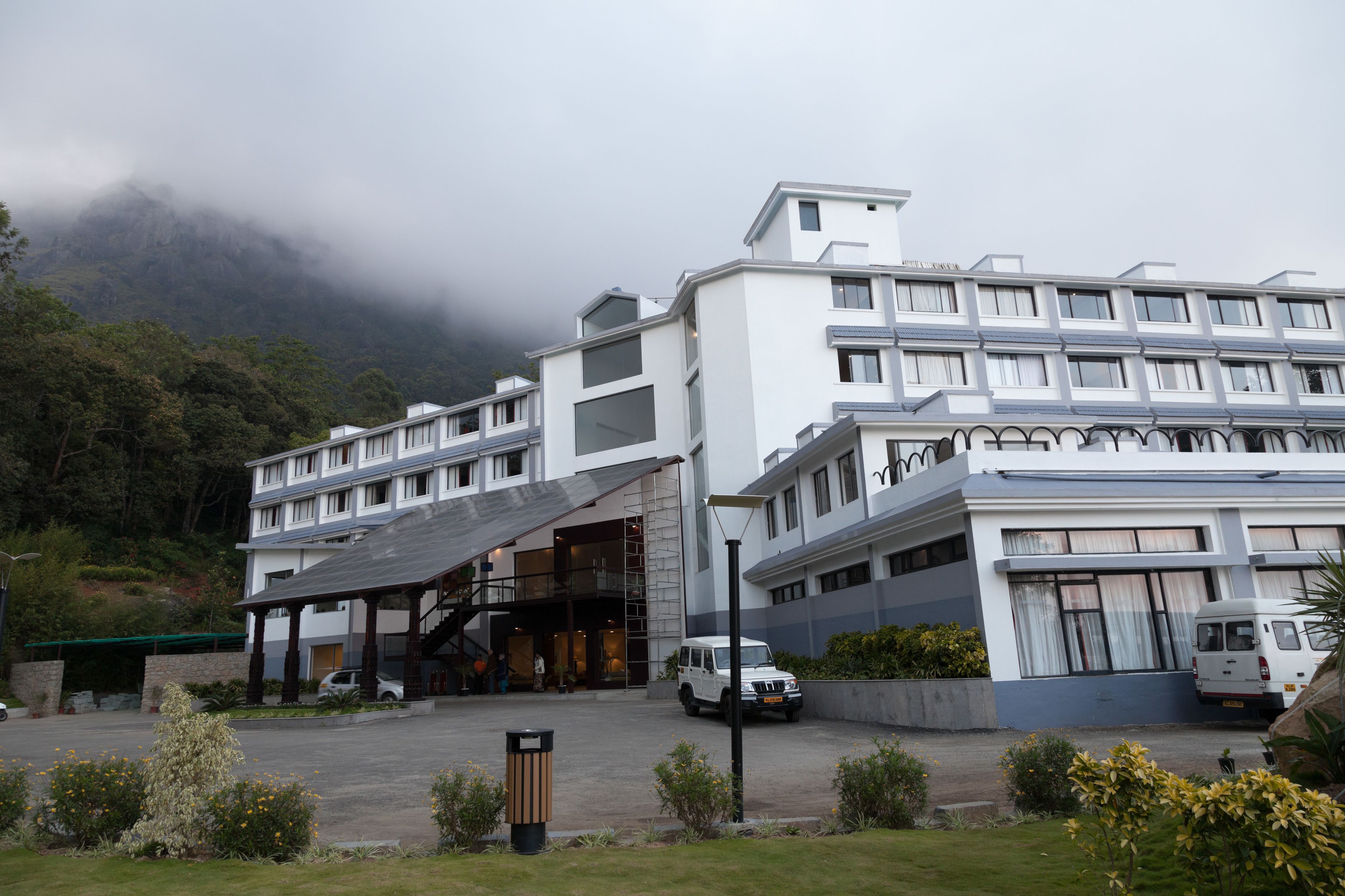 A modern hotel with multiple floors, a covered entrance, and a parking area with vehicles.
