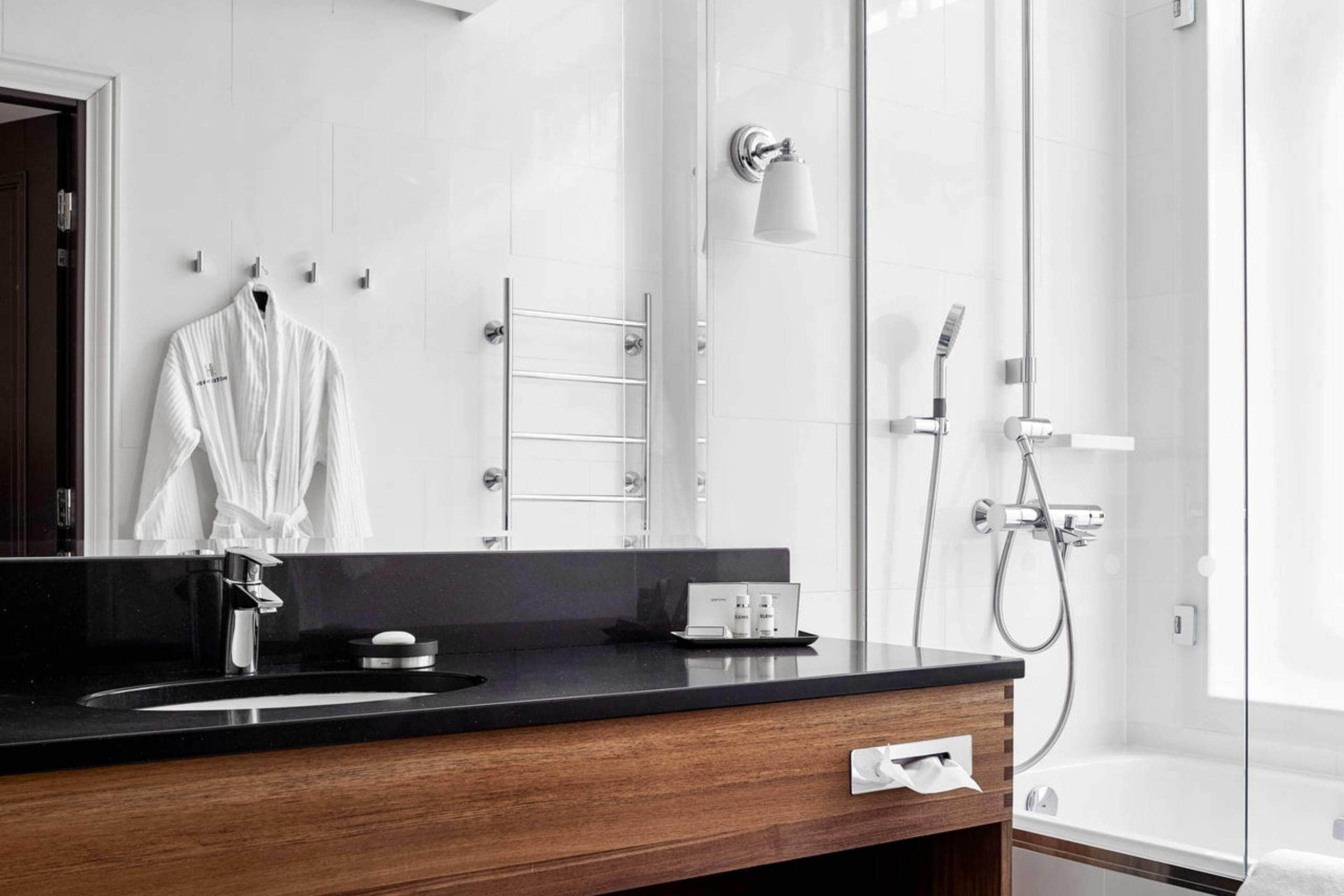 Un baño moderno con encimera negra, un espejo, una bata blanca colgada, cabina de ducha de cristal y una bañera.