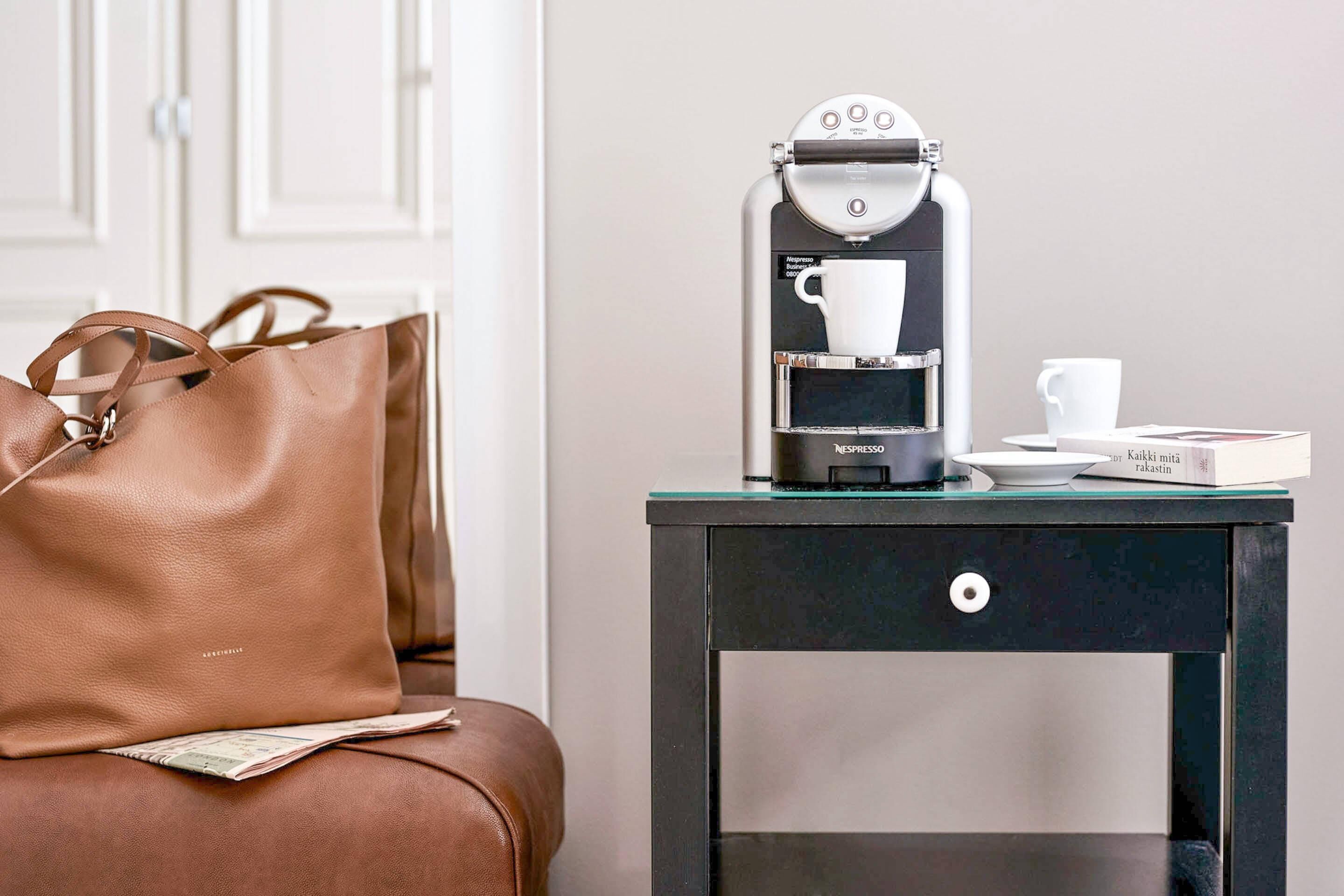 Una macchina da caffè su un tavolo con una borsa in pelle marrone e una rivista.