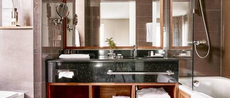 A modern bathroom with a dark marble sink, a glass-enclosed shower, and a wooden vanity with a mirror.