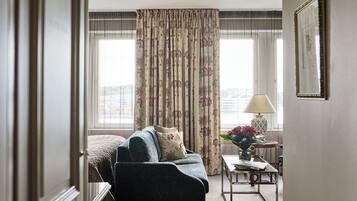 A hotel room with a sofa, a small table with a lamp, and a view through the window.