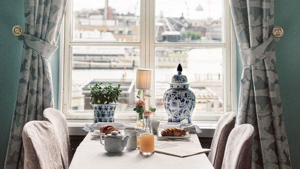 A breakfast setup with a table, chairs, and a view of a cityscape through a window. - Hotel Haven (Helsinki)