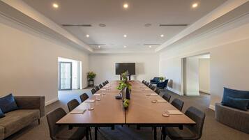 A conference room with a long table, chairs, a TV screen, and a potted plant.
