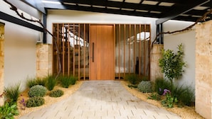 Una entrada moderna con puerta de madera, un corredor cubierto y un jardín con diversas plantas.