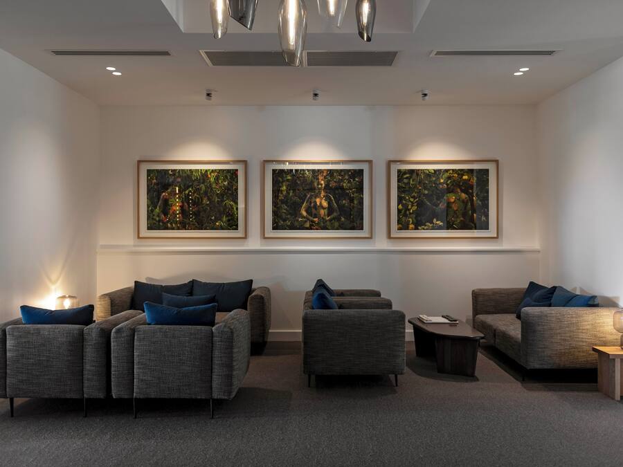A modern living room with grey sofas, blue cushions, and three framed artworks on the wall.