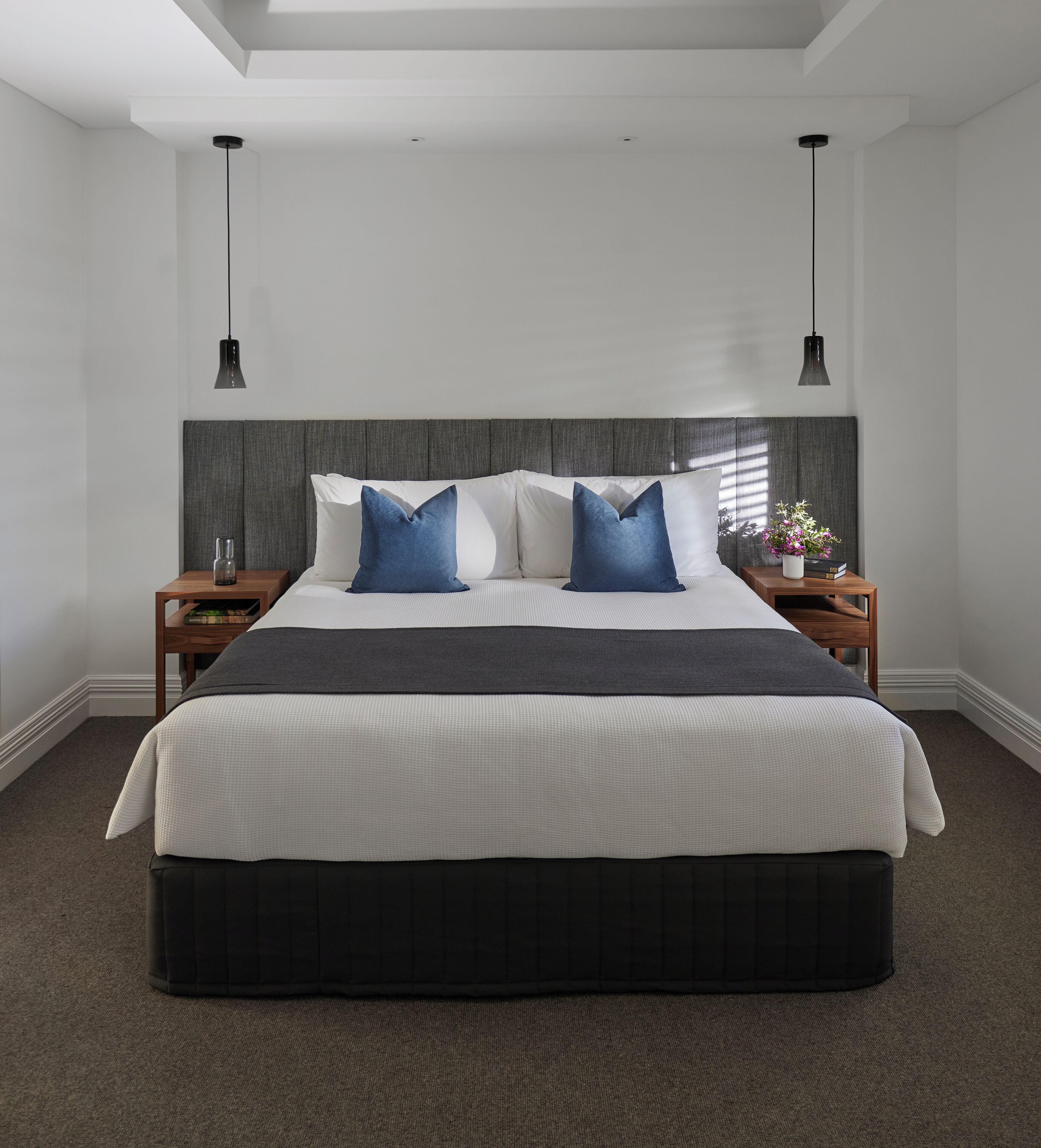 Een moderne slaapkamer met een groot bed, twee nachtkastjes en een grijs hoofdbord.