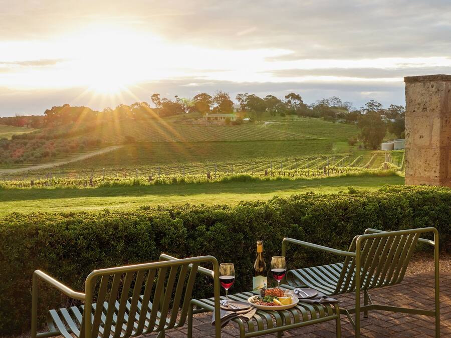 An outdoor seating area with two chairs and a table, set against a backdrop of a vineyard and a sunset.