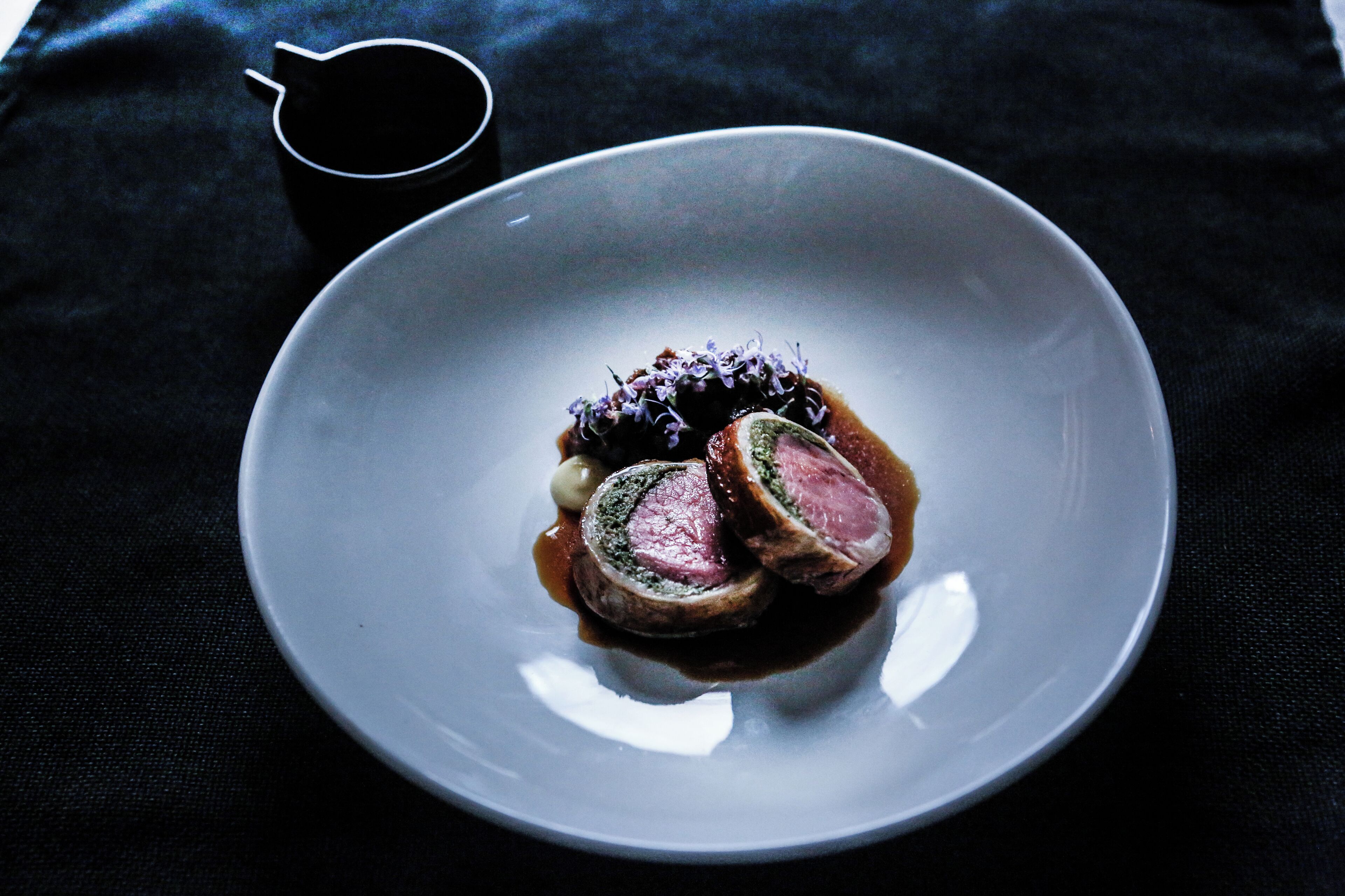 A plate with sliced meat and a sauce, placed on a dark cloth.