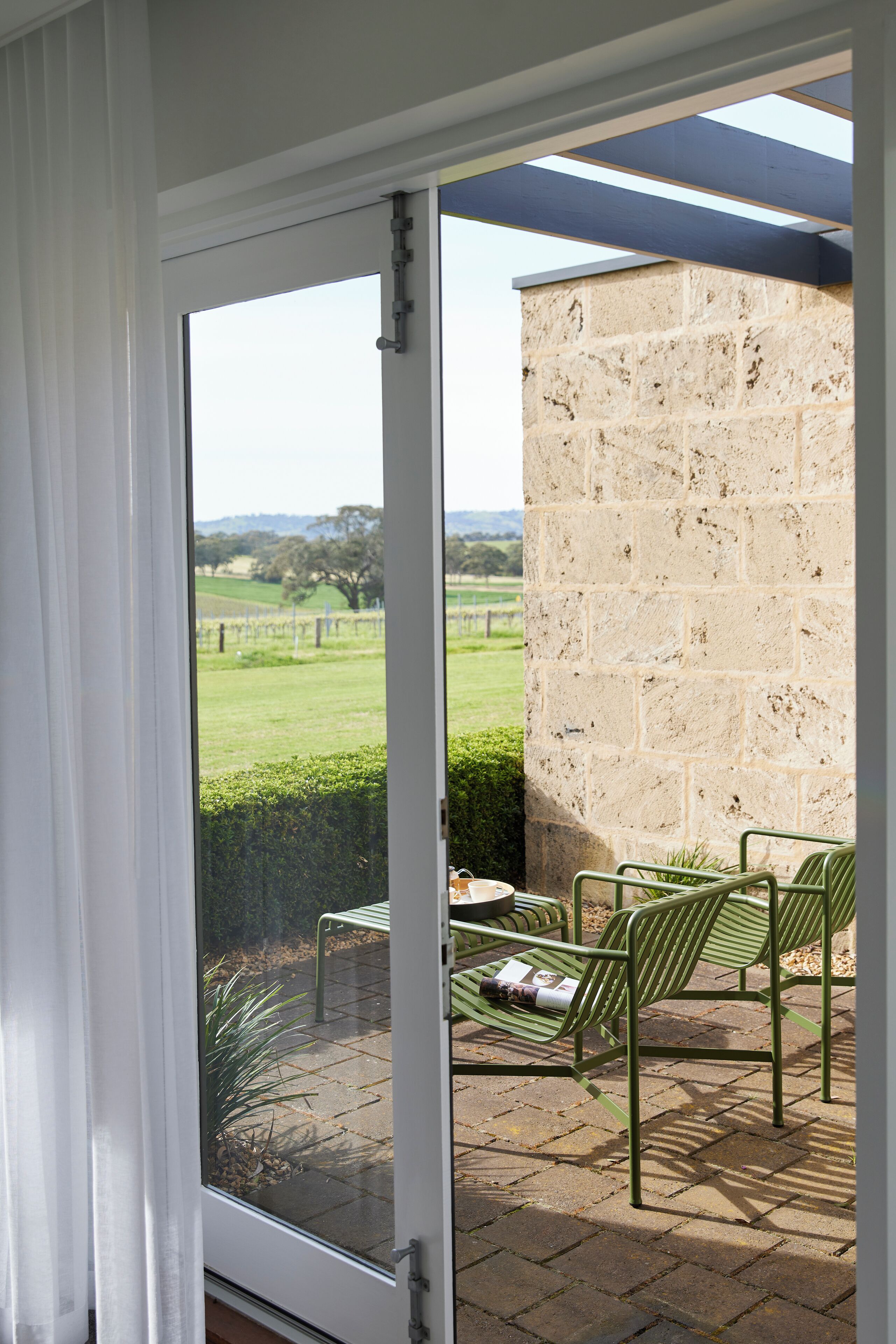 A patio with a stone wall, a glass door, and a view of a green landscape.