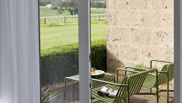 A patio with a stone wall, a glass door, and a view of a green landscape.