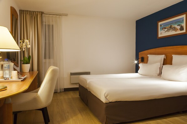 Una habitación de hotel con cama, escritorio con lámpara, silla y planta en maceta.