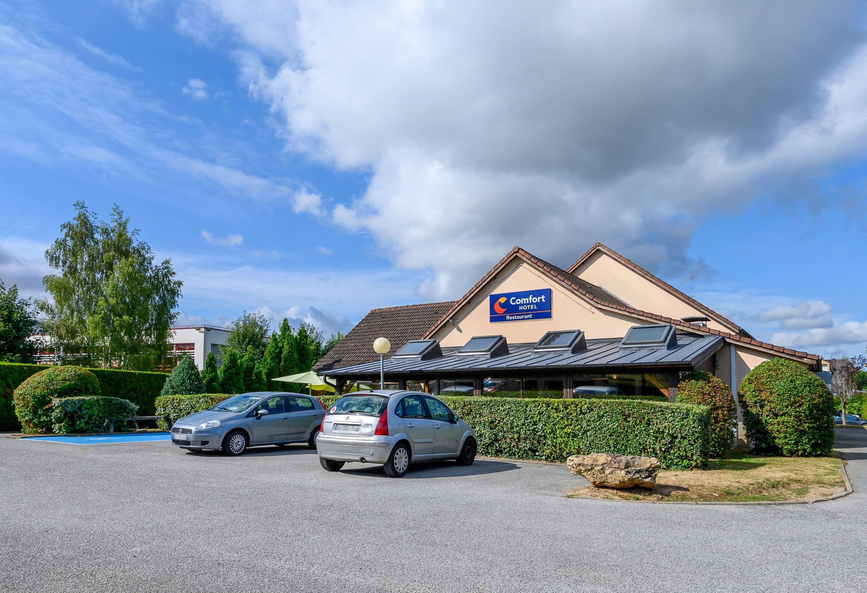 Restaurante de Comfort Hotel con aparcamiento, dos coches y un seto bien cuidado.